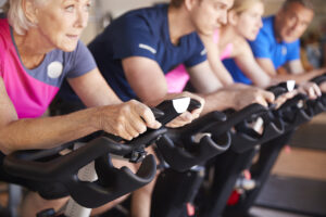 Group of people, including older adults, participating in a stationary cycling class.