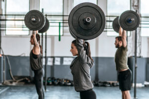 Athletes performing overhead presses during a CrossFit workout in a gym