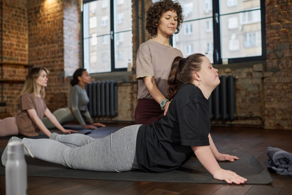 Instructor assisting a girl with a disability during a yoga class.